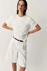 Camiseta blanca de algodón con cuello redondo, manga corta y detalle de flor en relieve bordada en el mismo tono.