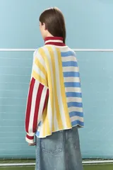 Sweater de punto de algodón con diseño de bloques de rayas verticales y horizontales en colores rojo, amarillo, azul y blanco. Presenta cuello alto con cierre frontal parcial y mangas largas con puños acanalados.