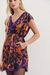 Vestido corto con escote en V y espalda semidescubierta. Presenta un estampado abstracto en tonos naranja, negro y violeta, con bordes a contratono en color violeta en el escote y el ruedo. Cuenta con cintura elástica y frunces en los hombros.