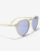 Lentes de sol Hawkers unisex, modelo Warwick Raw, con montura color marfil y lentes celestes.