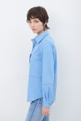 Camisa de estilo casual confeccionada en material tipo gamuza color marrón, con cuello clásico, cierre frontal con botones y costuras a la vista en tono contrastante.