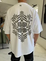 Remera oversize blanca con gran estampado en la espalda de diseño floral simétrico en tono oscuro. Cuenta con mangas cortas y calce holgado.