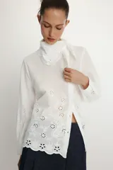 Camisa de manga larga en color blanco, confeccionada con detalles de bordados perforados a tono. Presenta un cuello tipo pañuelo y cierre frontal con botones.