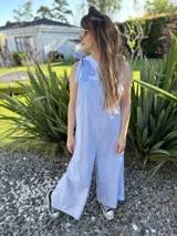 Mono largo de corte holgado con diseño de rayas verticales finas en azul y blanco. Presenta breteles anchos para atar sobre los hombros y piernas de corte ancho tipo palazzo.