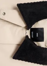 Chaqueta oversize color beige con cuello camisero de pana en contraste color negro. Presenta cierre frontal oculto con cremallera y botones, manga larga y bajo con cordón interior ajustable.