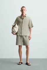 Bermuda negra de corte regular, confeccionada en tejido jacquard con efecto arrugado. Presenta cintura elástica ajustable con cordón blanco, bolsillos laterales y bolsillos traseros de vivo.