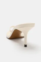 Sandalia de tacón fino medio, color blanco off-white, con diseño de tiras tipo thong para el dedo y punta cuadrada.
