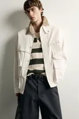 Parka relaxed fit de algodón color crudo, con cuello solapa marrón en contraste, múltiples bolsillos plastrón con solapa en el delantero y cierre frontal con cremallera y botones a presión.