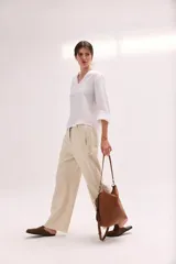 Pantalón de lino lavado color beige, de calce recto y diseño relajado. Presenta cintas de lino desflecadas aplicadas en los laterales con pespunte central, pretina con botón metálico, bolsillos delanteros y traseros.