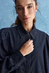 Camisa de jean azul oscuro con calce relajado, cuello clásico, bolsillo aplicado en el delantero y mangas largas abullonadas con puños abotonados.
