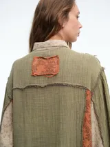 Vestido camisero de corte midi con diseño patchwork que combina paneles en tonos crudo y marrón con estampados florales sutiles. Presenta cierre frontal con botones, cuello camisero y mangas largas con puños.