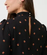Vestido corto negro de chiffon con estampado de pequeños corazones naranjas, cuello alto, mangas largas abullonadas y falda con volados en capas.