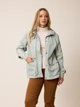 Campera de estilo parka en color verde menta claro, con capucha ajustable, cierre frontal con botones a presión y bolsillos frontales con solapa. Presenta un diseño funcional con puños ajustables y forro interior.