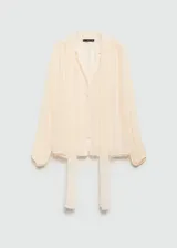 Blusa de viscosa color crema, con diseño semitransparente, cuello con lazada, mangas largas abullonadas y cierre frontal con botones.