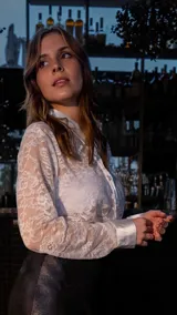 Camisa blanca de encaje con cuello camisero y mangas largas con puños combinados en satén. Cierre frontal con botones.