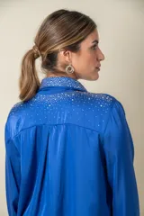 Camisa color crema de satén italiano con cuello clásico, cierre frontal con botones y mangas largas. Presenta apliques de strass en cuello, solapa y puños.