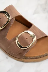 Sandalias marrones de cuero con dos tiras anchas ajustables con hebillas doradas. La plantilla es de corcho y la suela es de goma.