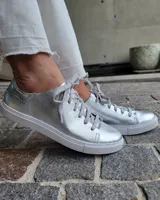 Zapatillas plateadas de cuero con cordones grises y suela blanca.