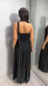 Vestido largo negro strapless con falda translúcida y detalle de bufanda o lazo integrado al cuello.