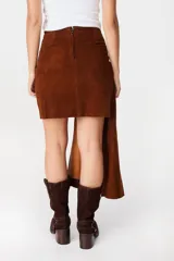 Falda de cuero marrón con diseño asimétrico, presenta un detalle de lazo frontal drapeado que crea una caída lateral más larga.