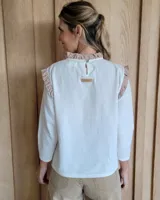 Blusa blanca de manga larga con cuello alto y volados en cuello y hombros.