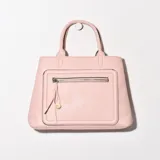 Cartera rosa de simil cuero con doble asa corta, bolsillo frontal con cierre y detalle de borla.