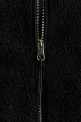 Chaleco de sherpa color negro con cuello elevado y cierre frontal. Presenta ribetes de cinta en los bordes, bolsillos tipo parche en la parte delantera y forro interior.