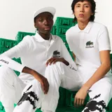 Chomba blanca de piqué de algodón con cuello clásico y tapeta de dos botones. Presenta logo de Lacoste y cocodrilo pixelado de Minecraft bordados en el pecho.