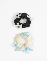 Set de dos gomitas para el pelo tipo scrunchie, una negra con moños blancos y otra color crema con moños celestes.