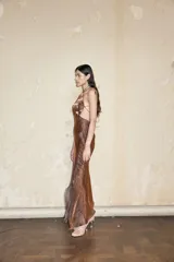 Vestido largo de organza italiana color negro con acabado laminado. Presenta un escote halter con diseño de corazón, aberturas laterales tipo cut-out y falda fluida con bajo asimétrico. La espalda es descubierta con cierre de cordones entrecruzados.