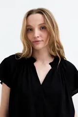 Blusa de manga corta color negro, con escote en V y frunces en los hombros, de diseño holgado y ligero.