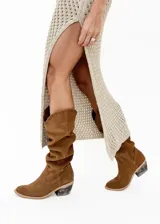 Bota tejana de caña alta color tostado, confeccionada en cuero vacuno. Presenta tiento cosido a mano en la parte superior y taco de 4 cm.