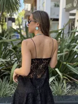 Top negro de encaje con breteles finos, detalle fruncido en el escote y abertura frontal cubierta por un nudo.