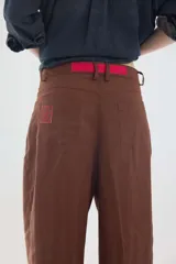 Pantalón de lino marrón de tiro medio, con calce holgado y diseño de piernas amplias. Cuenta con bolsillos traseros, trabillas para cinto y un pin bordado en contraste.
