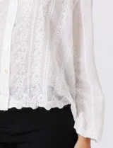 Camisa de algodón blanca con bordados florales verticales, cuello con solapa y cierre frontal con botones.