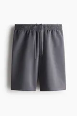 Short de felpa interlock color gris oscuro, con cintura elástica fruncida y cordón ajustable. Presenta un diseño de corte relajado a la rodilla, bolsillos laterales y bolsillos traseros.