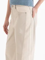 Pantalón de cuero color beige, de corte recto y holgado, con detalles de tejido texturizado en los laterales y bolsillos.