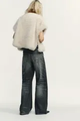 Chaleco Zara de pelo sintético en color beige, con diseño abierto, manga muy corta y cierre lateral con clip.