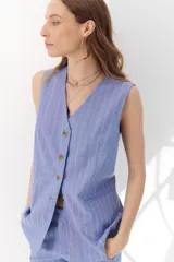 Chaleco largo color blanco con rayas verticales finas color beige, con cuello en V y cierre frontal con botones marrones. Incluye pañuelo al cuello con estampado de lunares y rayas.