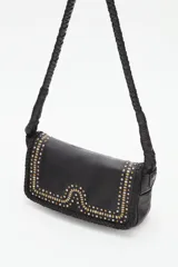 Cartera tipo baguette de cuero vacuno negro, con detalles de tachas metálicas doradas y plateadas en la solapa y borde trenzado. Cuenta con una correa de hombro trenzada.
