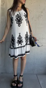 Vestido corto blanco con estampado de flores negras, corte suelto y ruedo con volantes.