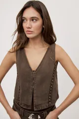 Chaleco corto de denim negro con escote en V y diseño sin mangas. Presenta terminación lavada y detalles laterales con entramado y tachas metálicas que aportan un toque distintivo.