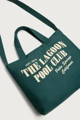 Bolso tipo shopper verde oscuro de tejido de algodón, con doble asa de mano y estampado frontal en color beige con la inscripción "The Lagoon Pool Club Palm Springs California".