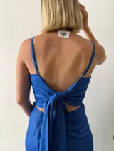 Conjunto de dos piezas en lino con lurex color azul brillante. Incluye una falda corta cruzada con volados y un top halter con escote recto y lazo ajustable en el contorno.