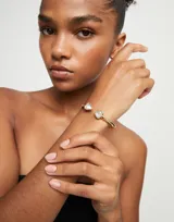 Pulsera rígida dorada de aleación de metales bañada en oro 18k, con dos cristales facetados multicolor en forma triangular en los extremos.