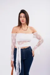 Blusa de encaje blanco con diseño off-shoulder, mangas largas acampanadas y detalle de lazo frontal para anudar en la cintura.