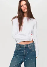 Jeans de tiro medio y corte barrel con diseño de ojales metálicos distribuidos por toda la prenda. Cuenta con cinco bolsillos, cierre de botón y cremallera, y trabillas para cinturón.