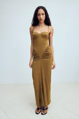 Vestido largo color tostado con diseño estilo corsé, escote corazón con aros y tirantes finos. Presenta un corte ajustado en la cintura con detalle de frunces laterales que aportan volumen a la falda.