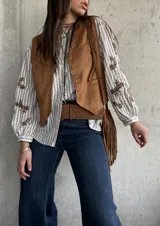 Chaleco de gamuza color camel forrado, con ribetes decorados con tachas metálicas y tiras colgantes con flecos en el lateral.