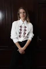 Camisa de algodón con corte clásico, cuello camisero y mangas largas con puños abotonados. Presenta un bordado geométrico en color bordó en la parte frontal y detalle de frunce en la espalda.